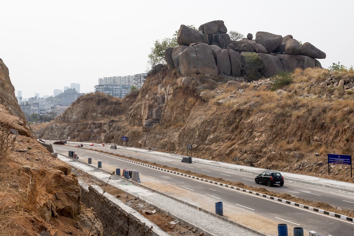 A new road cuts through hills with rock formations near Hyderabad's Maulana Azad National Urdu University.