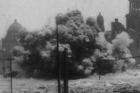 A dynamite blasts in front of the damaged City Hall. 