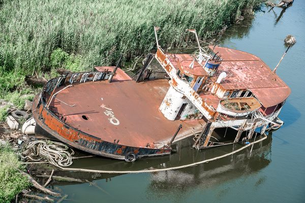 A rusty ship sits on a grassy riverbank.