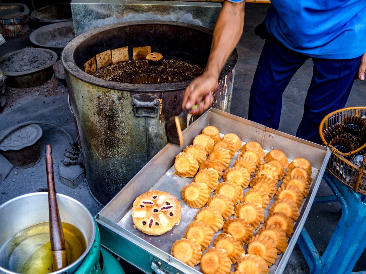 A baker at Kanoom Farung Lan Mea Pao picks freshly baked cakes out of the charcoal brazier and moves them to a metal box to cool.