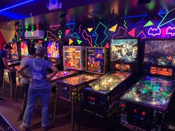A blacklight- and neon-lit wall of pinball machines at Seven’s Pinballorama