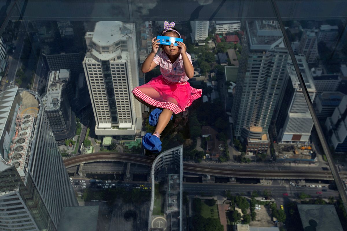 A girl observes a partial solar eclipse on the Mahanakhon Skywalk Glass Tray in Bangkok, Thailand (June 2020).