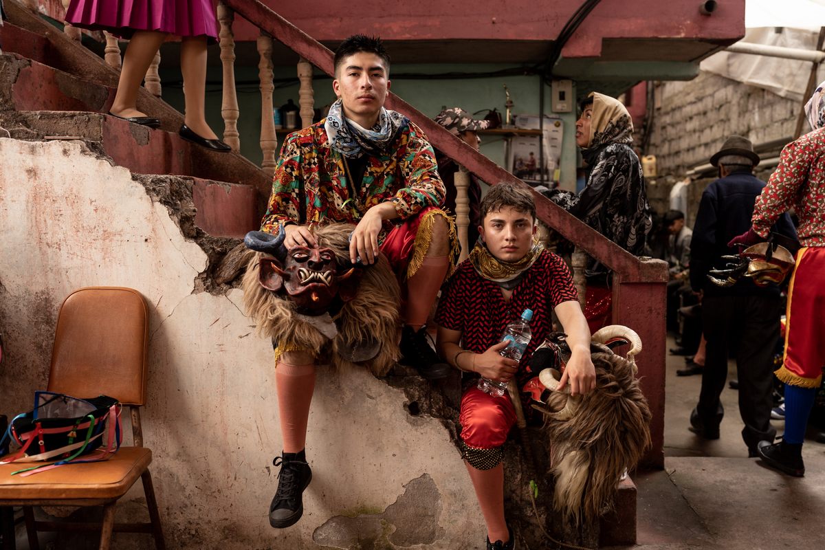 Two members of the Minga Tunguipamba sit on a set of stairs while the group rests, eats, and drinks before parading back to their community beyond the city.
