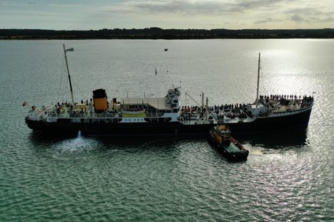 The Shieldhall, assisted by a tug, is silhouetted by the afternoon sun
