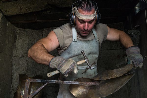 Dimitrios Katsikis bangs away with a hammer, which he crafted himself from scrap metal, to shape a bronze greave, or shin guard. One of the very few modern technologies he allows himself is ear protection. 