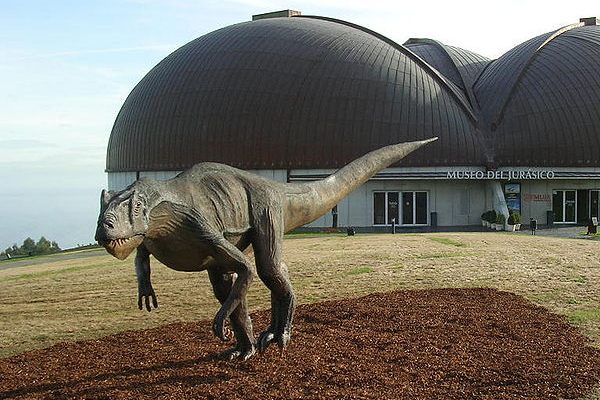 Lifesize model of Allosaurus with the museum in the backdrop.
