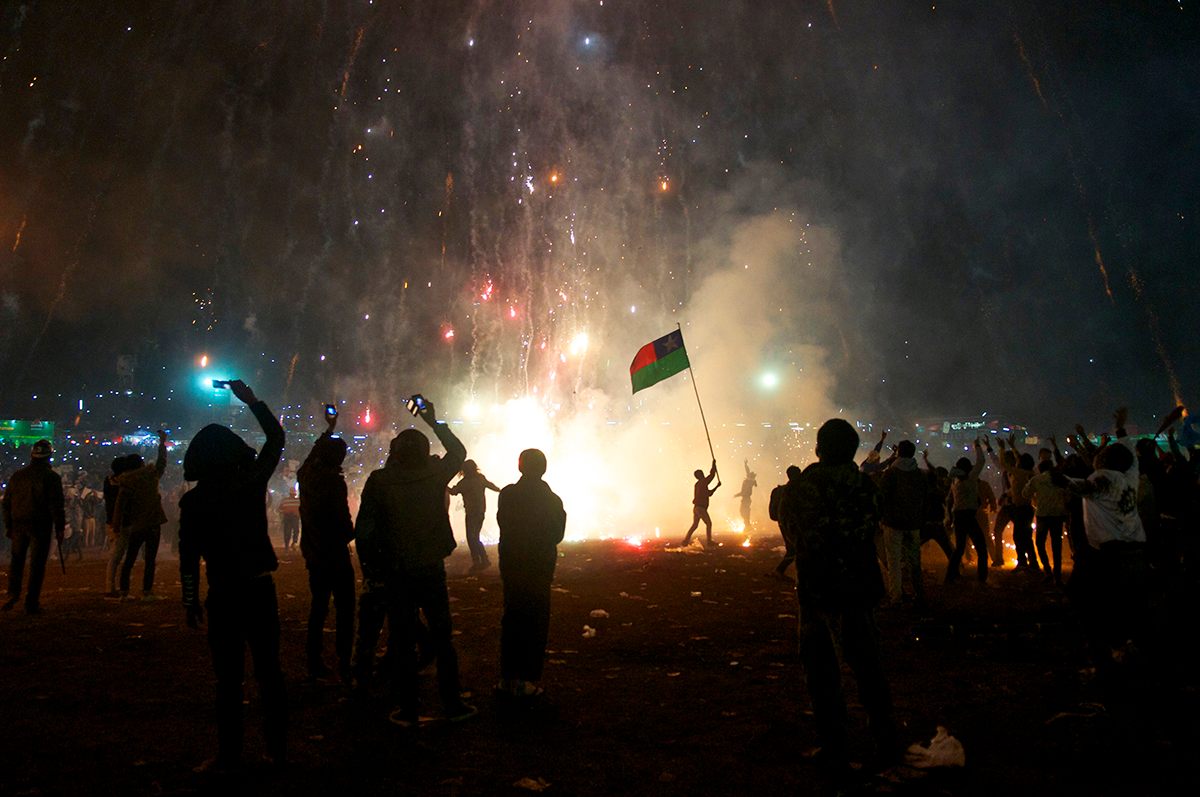 A man waves a Pa'oh flag as a hot-air balloon takes off. Fireworks attached to its base shoot down onto spectators.