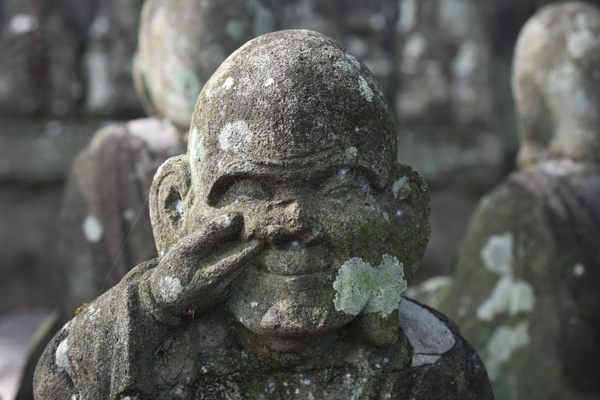 A worn statue of a Japanese monk picks his nose.