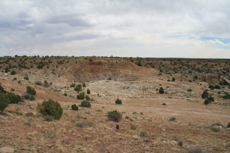 Looking southeasterly over the main experimental site.  The chain-link fence around the main shaft can be made out just up and to the right of center.  The edge of the large crater made by one of the biggest surface blasts is visible behind.