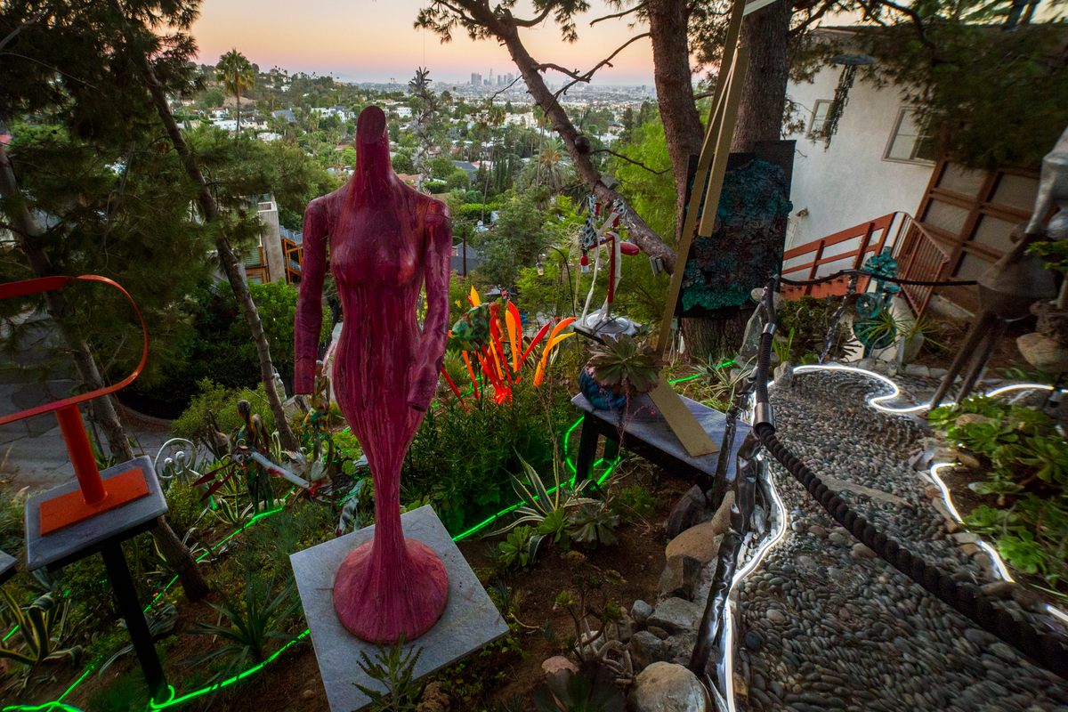 A woman-shaped sculpture stands in front of a cinematic sunset.