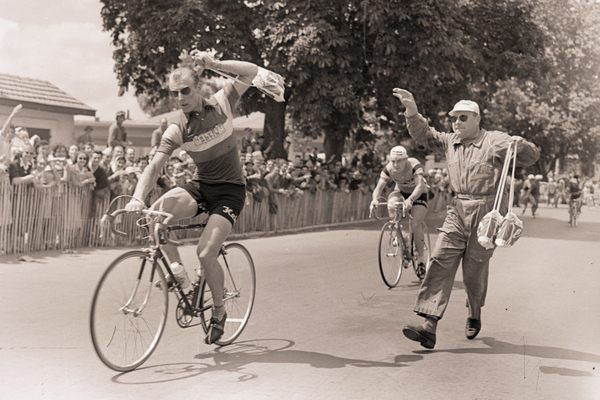 A soigneur performs a successful musette handoff to cyclist Andre Darrigade in 1956.