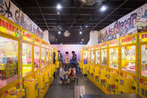 In the back, men play. A child watches patiently on the bench as his mother, a renter of claw machines, reorganizes the prizes. 