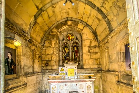 The small interior of a chapel with a small mosaic floor arched roof and two coffins.