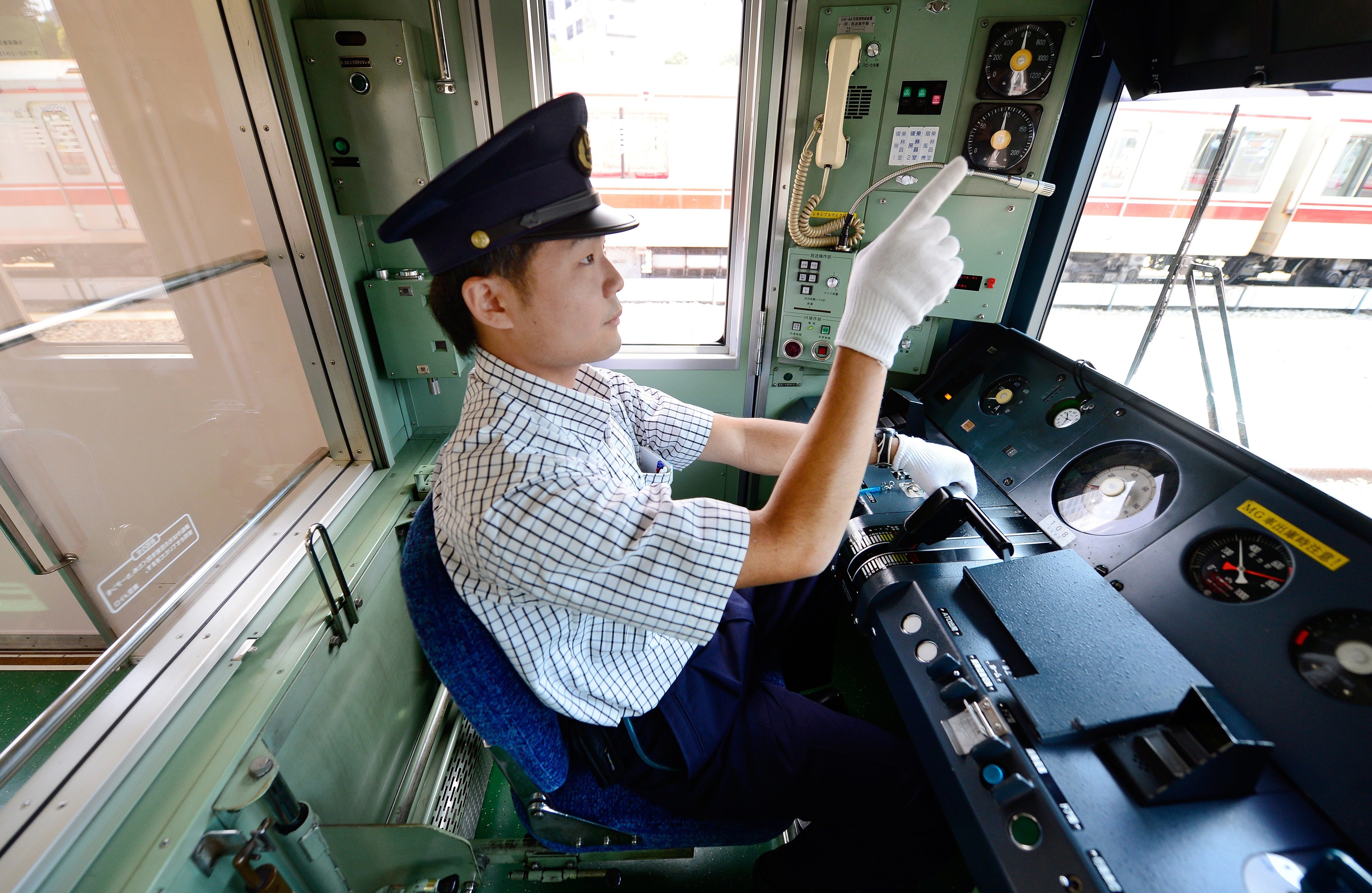 A Tokyo train driver pointing at meters on the dashboard.