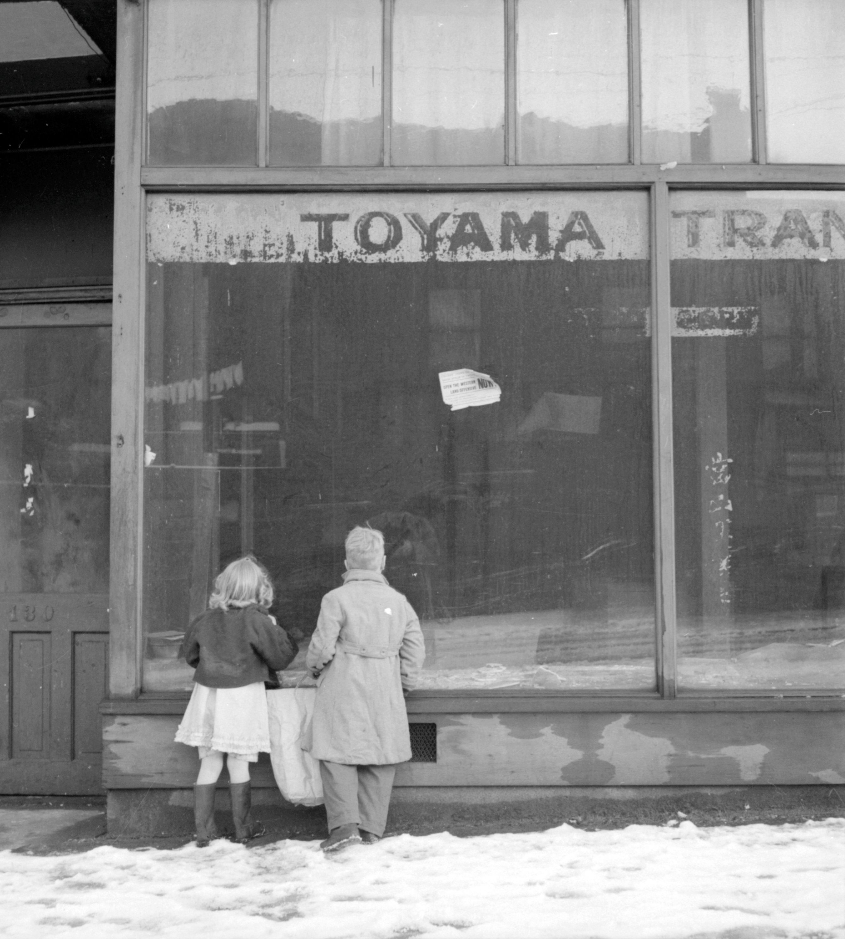 Two children look into the window of a store, closed after the forced relocation of Japanese Canadians.