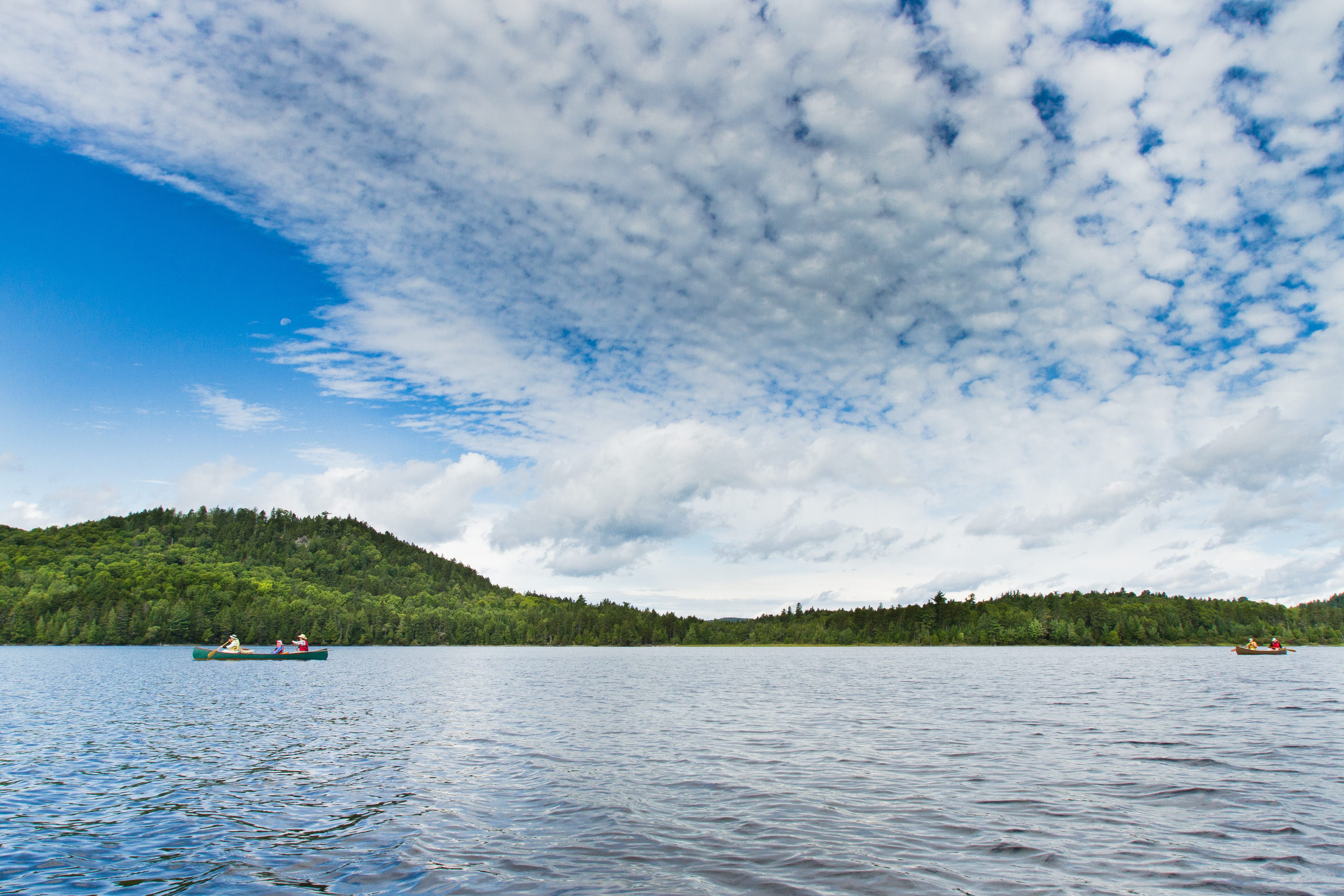 People paddling in their wooden canoes on one of the lakes near the Allagash Waterway in the north woods in Maine