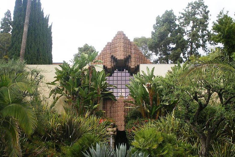 The Sowden House's geometric, Mayan-inspired stone facade rises above a lush garden of tropical plants and palms.