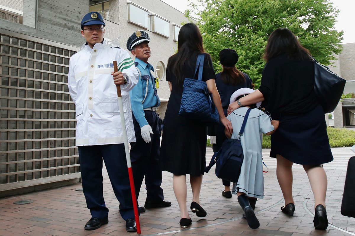 Children arrive at an elementary school in Kawasaki with their parents not long after a knife-wielding intruder had attacked there. One of the guards carries a bo staff. 
