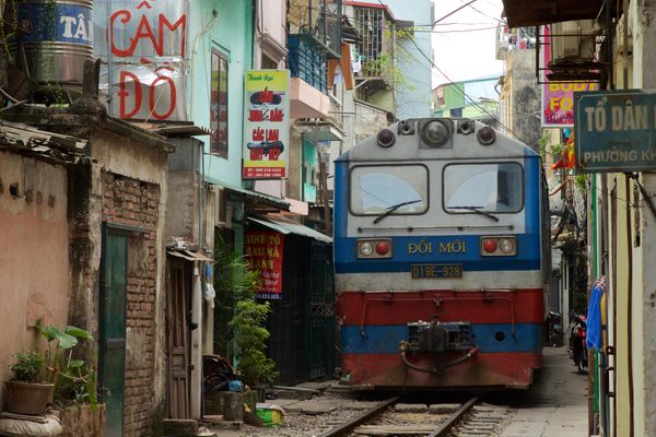 Diesel train coming down the train tracks through a narrow street in Hanoi.