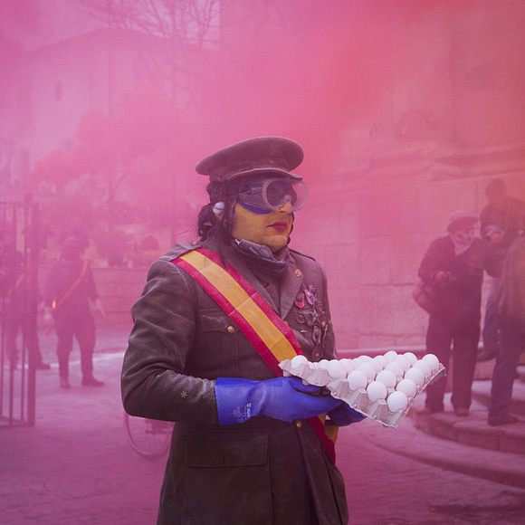 Amidst colored smoke bombs, a mock soldier prepares to throw eggs.