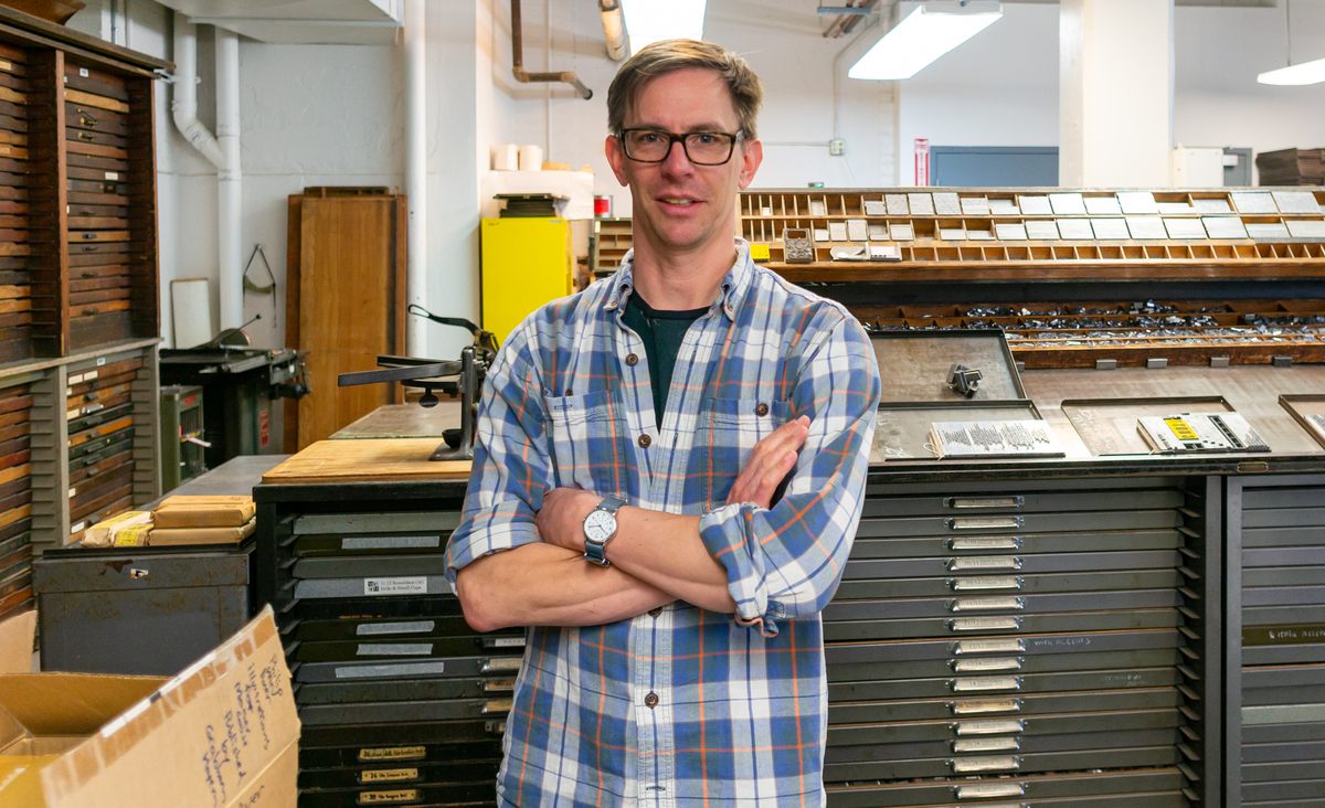 Brian Ferrett stands in front of cases cabinets of type. He began as an apprentice type-caster 11 years ago, and now runs the facility.
