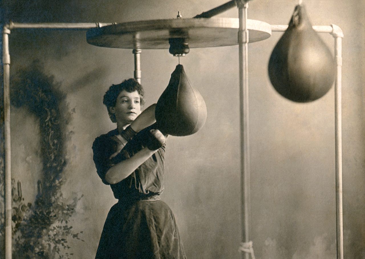 A young woman working out using boxing gloves and a punching bag in 1890.