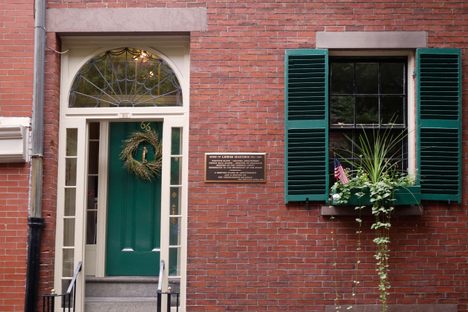 A brick colonial home with a green door and a green-shuttered window
