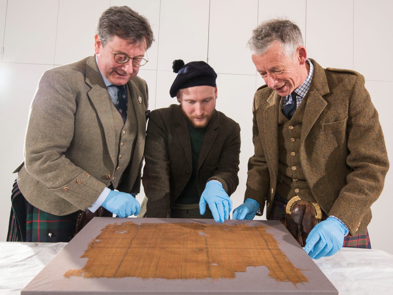 John McLeish, chair of the Scottish Tartans Authority; curator James Wylie; and Peter MacDonald (right), STA tartan historian (left to right), examine the Glen Affric tartan. 