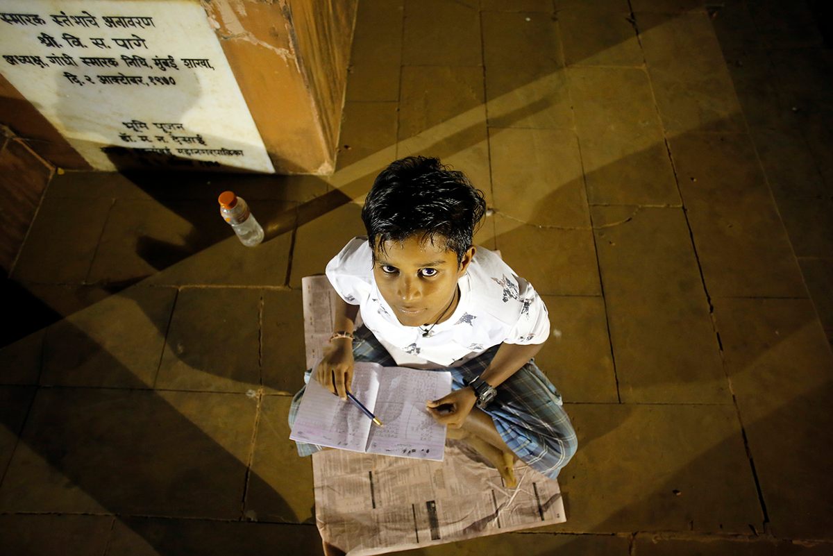 A student named Vivek Kharwa does schoolwork at August Kranti Maidan.