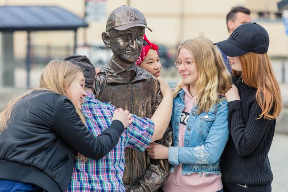A group of teenagers hug a bronze statue with a baseball cap