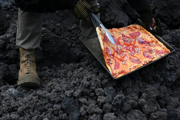 David García checks a pizza he is cooking on a Pacaya lava river in May, 2021.