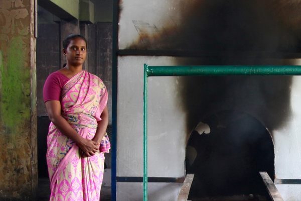 Crematorium assistant Divya Raju and a furnace operator pose in front of an active furnace.