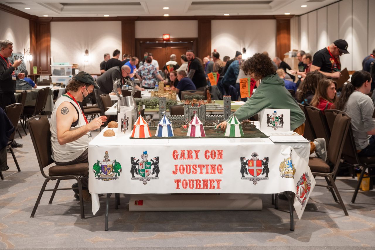 Two Gary Con participants play a tabletop jousting game similar to rock-paper-scissors.