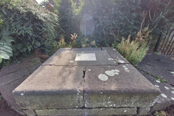 A stone slab with a plaque surrounded by a garden and fence.