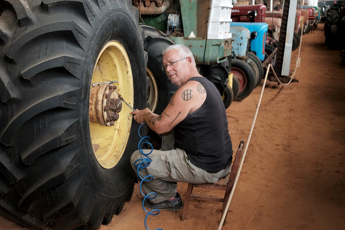 Museum founder Erez Milstein works on repairing a tractor's wheel. The tattoos on his arm represent the spare parts needed to restore many of the machines.