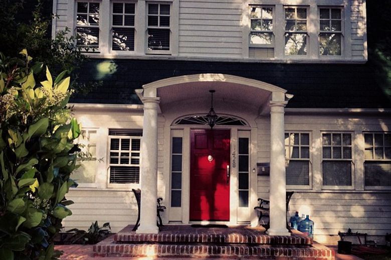 The front entrance of a white two-story house featuring a bright red door under a columned portico.