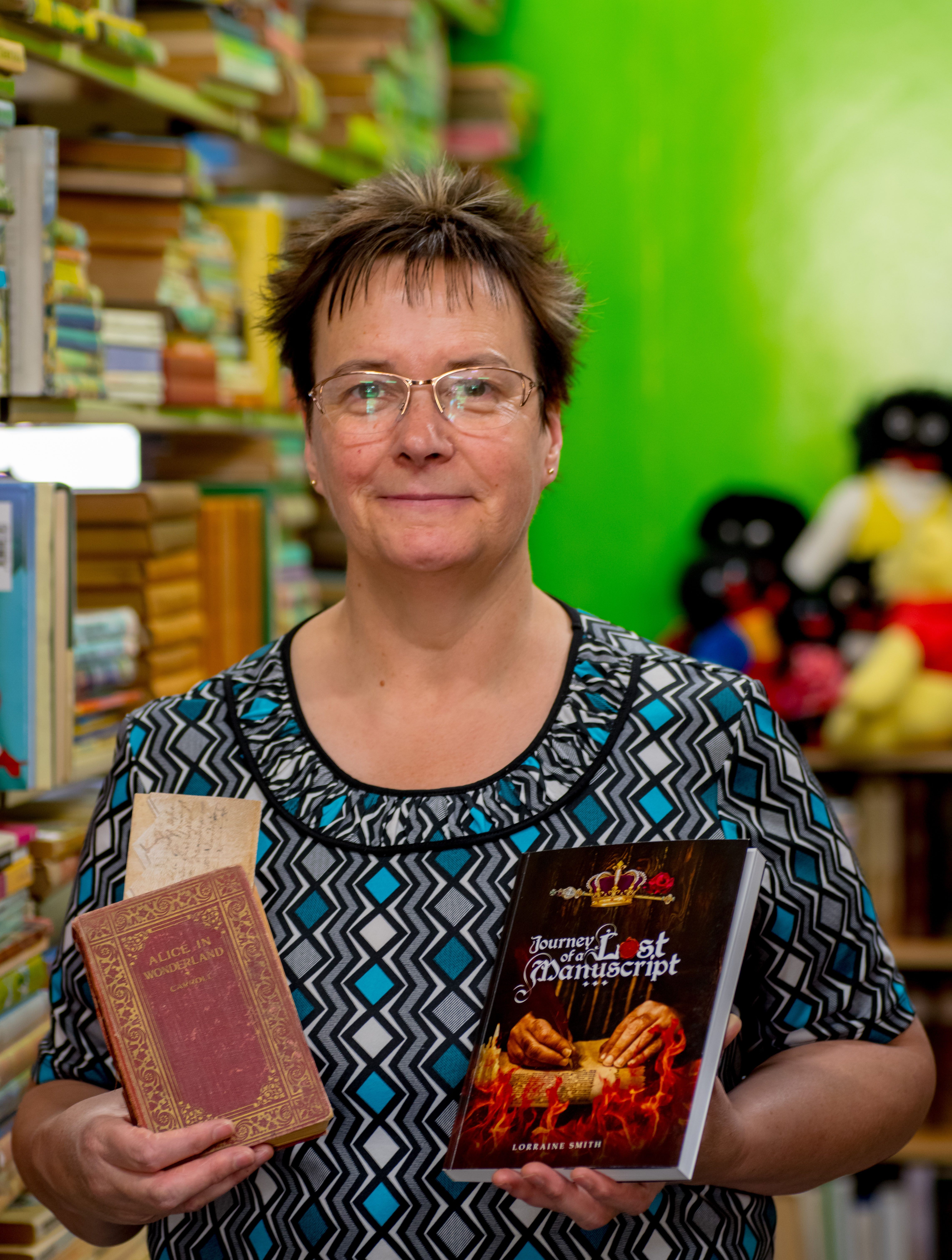 Lorraine Smith in her shop with the deed, <em>Alice in Wonderland</em>, and her own book about her investigation.