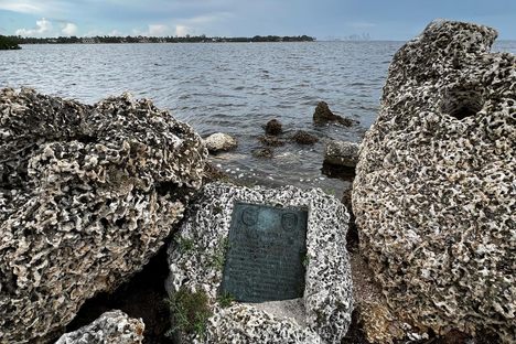 A bronze plaque embedded into a rock alongside other rocks with the sea behind it