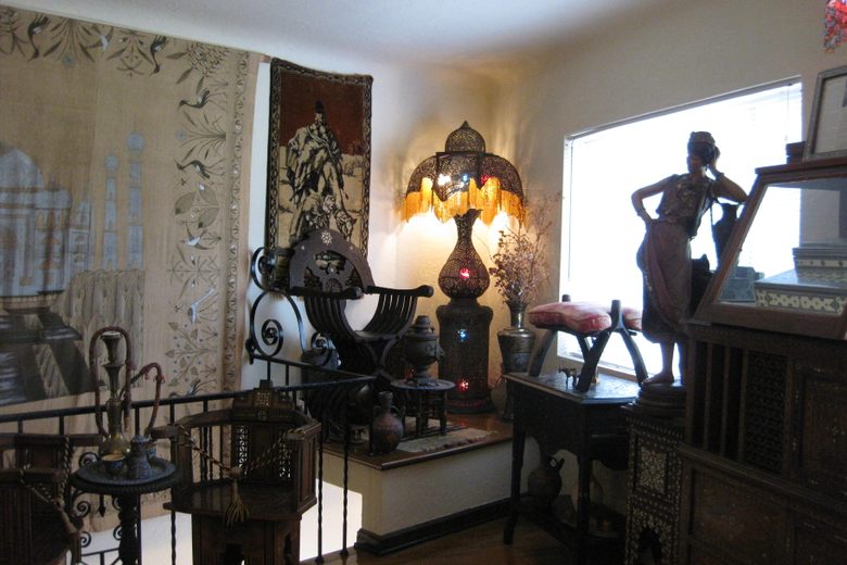 A room filled with Middle Eastern artifacts, including ornate wooden chairs, tapestries, and a glowing filigree lamp.