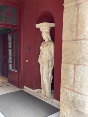 A plaster column shaped like a woman in robes sits in a red niche