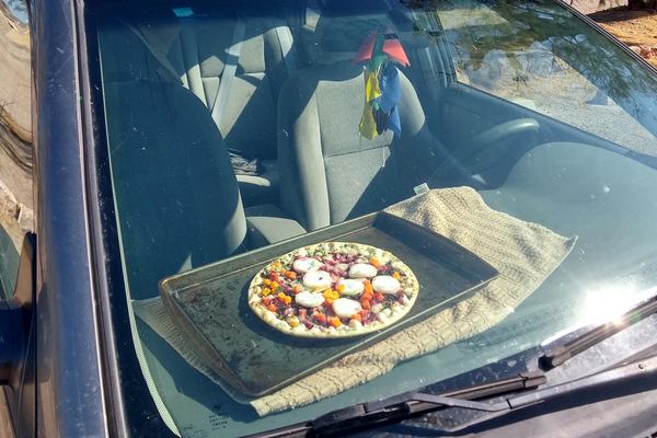 在死亡谷国家公园，一名披萨厨师坐在一辆汽车的仪表盘上。夏天，气温通常会达到华氏120度。