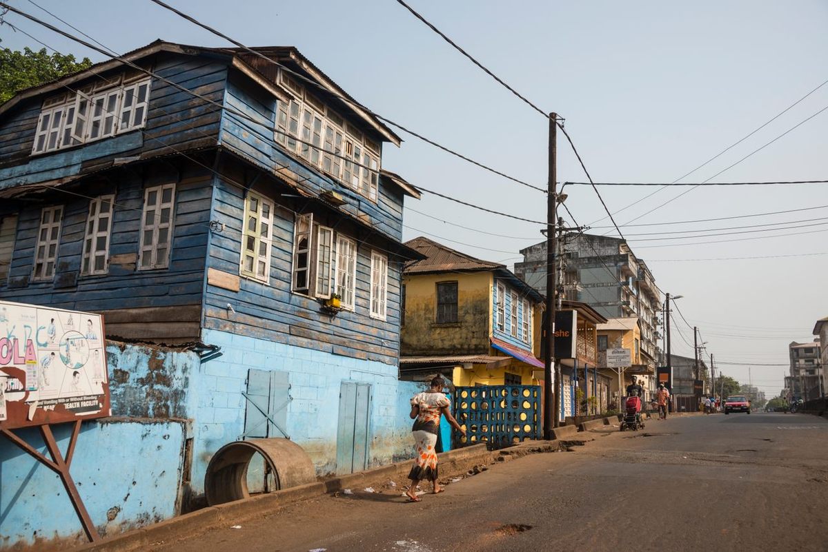 A blue Krio house, also known as a <em>bod os</em>, stands over a quiet Freetown street.