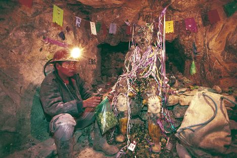 A miner sits at the feet of El Tio, leaving offerings for safety and prosperity.