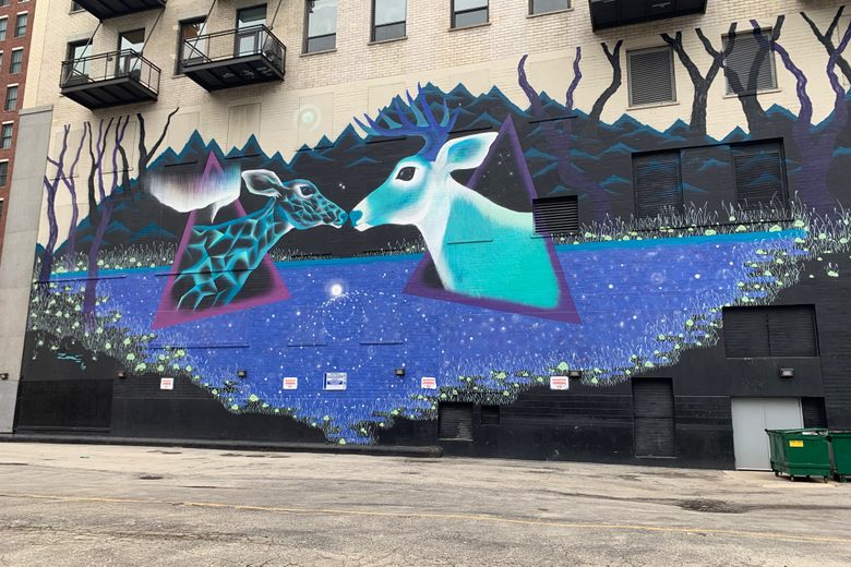 A large mural on a brick building depicts two stylized blue and teal deer facing each other over a starry blue lake.