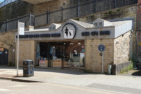 A museum entrance with sliding glass doors below a sign in blue letters that says "Stockport Air Raid Shelters"