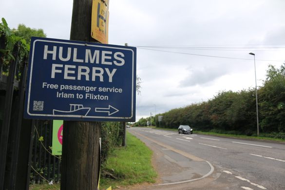 A blue sign with "Hulmes Ferry" next to a roadway