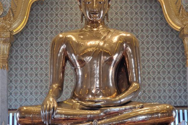 Golden Buddha sits in on a marble pedestal.