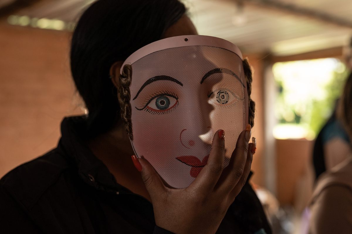 A woman holds a fair-skinned, blue-eyed mesh mask of a <em>bailarine de línea</em>, or line dancer.