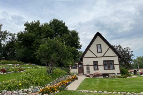 A tudor style A-frame house set in a picturesque garden with a manicured lawn and rock walls.