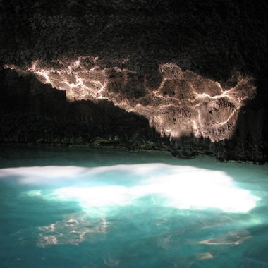 Sunlight from the dome's opening plays on the surface of the spring water, reflecting on the rock face inside